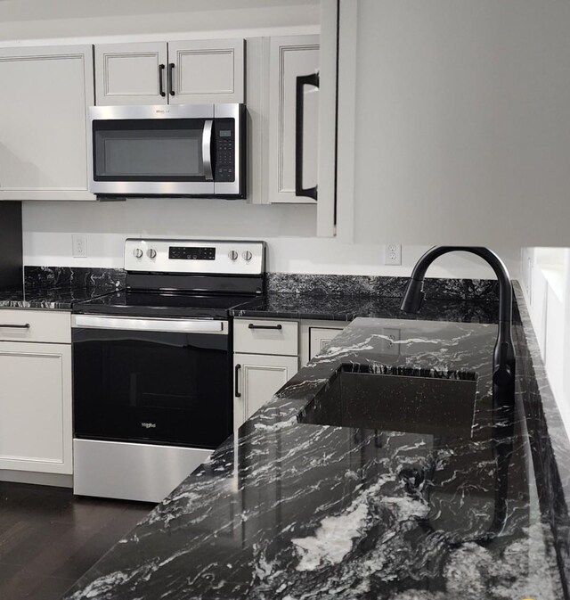 kitchen with white cabinets, sink, dark wood-type flooring, appliances with stainless steel finishes, and dark stone countertops