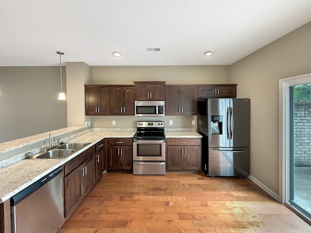 kitchen with dark brown cabinetry, pendant lighting, sink, stainless steel appliances, and light wood-type flooring