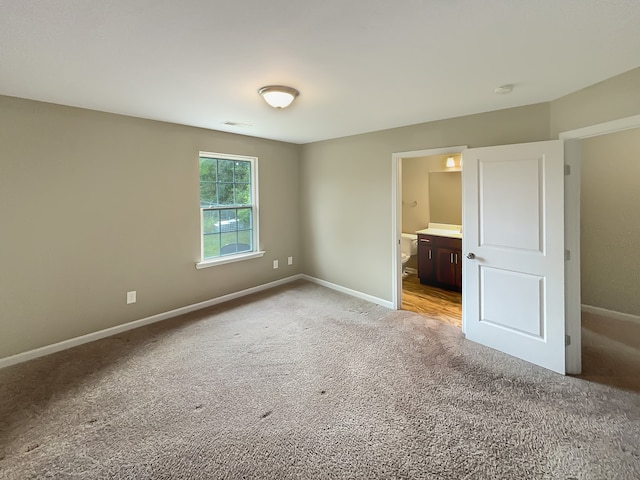 unfurnished bedroom featuring ensuite bath and light colored carpet