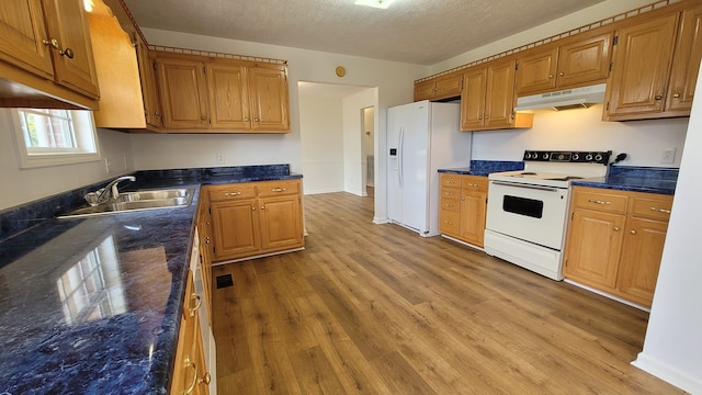 kitchen with white appliances, sink, light hardwood / wood-style floors, dark stone counters, and a textured ceiling