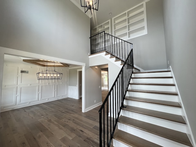 stairway featuring a towering ceiling, an inviting chandelier, and hardwood / wood-style flooring