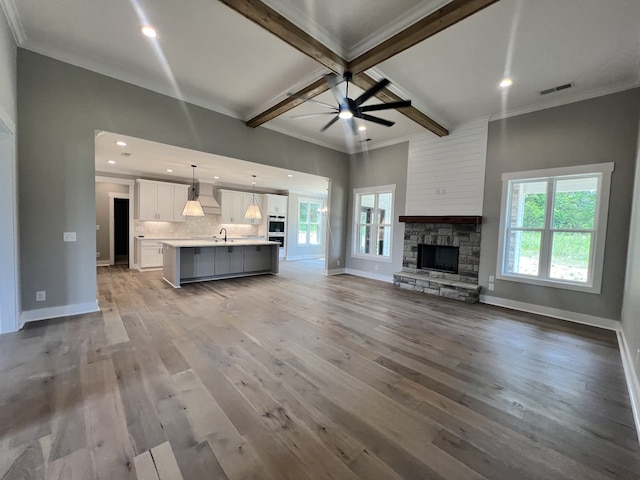 unfurnished living room with wood-type flooring, beam ceiling, ceiling fan, and a fireplace