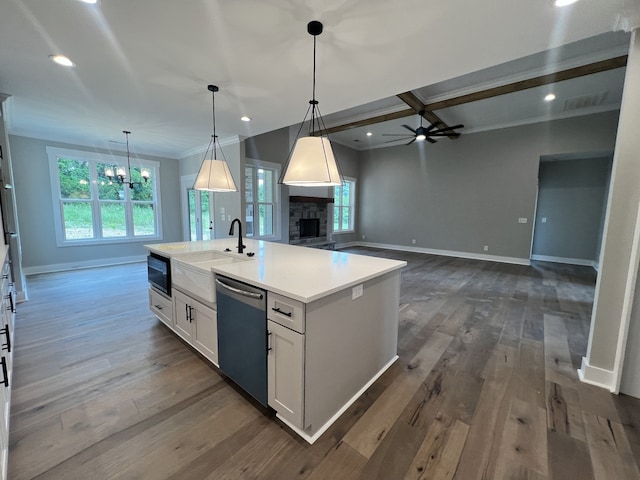 kitchen with an island with sink, white cabinets, ceiling fan with notable chandelier, a fireplace, and stainless steel dishwasher