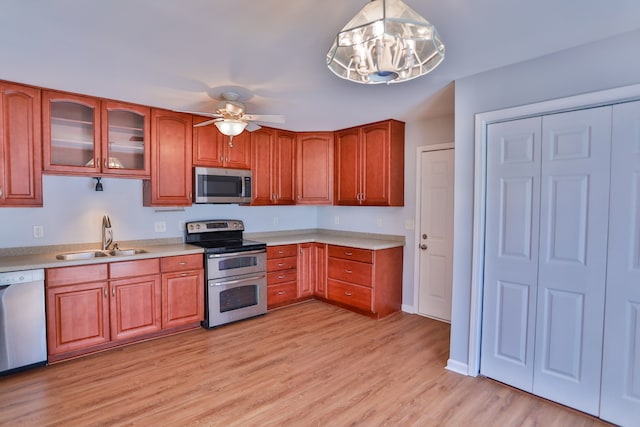 kitchen with stainless steel appliances, light hardwood / wood-style floors, sink, ceiling fan with notable chandelier, and pendant lighting