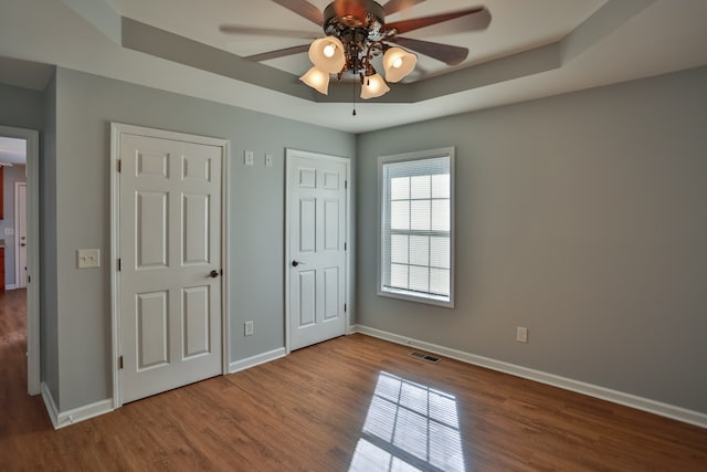 unfurnished bedroom featuring hardwood / wood-style floors, ceiling fan, a raised ceiling, and two closets