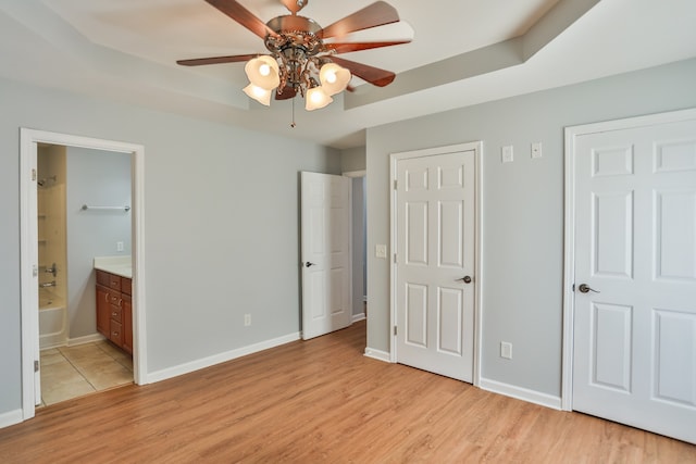 unfurnished bedroom with light hardwood / wood-style flooring, a raised ceiling, ceiling fan, and ensuite bath