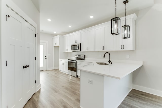 kitchen featuring white cabinets, sink, hanging light fixtures, light hardwood / wood-style flooring, and stainless steel appliances