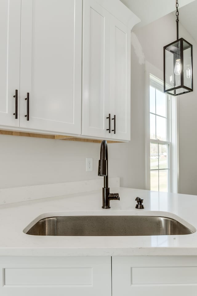 kitchen with light stone countertops, white cabinetry, hanging light fixtures, and sink