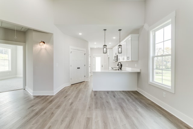 kitchen with kitchen peninsula, light wood-type flooring, sink, white cabinets, and hanging light fixtures