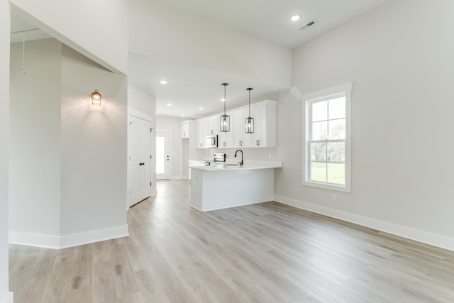 kitchen featuring white cabinets, sink, hanging light fixtures, light hardwood / wood-style floors, and kitchen peninsula