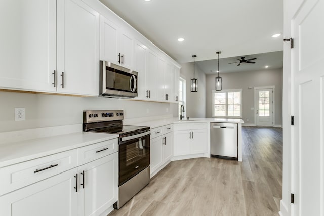 kitchen with kitchen peninsula, appliances with stainless steel finishes, ceiling fan, sink, and light hardwood / wood-style flooring