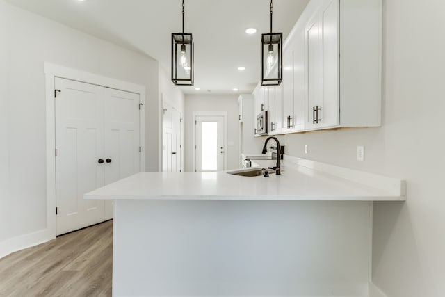 kitchen featuring white cabinets, sink, light wood-type flooring, decorative light fixtures, and kitchen peninsula