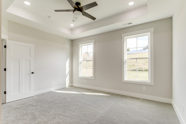 spare room with ceiling fan, a raised ceiling, and light colored carpet