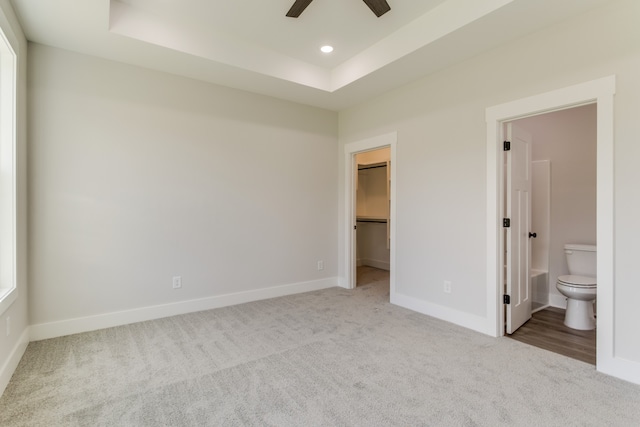 unfurnished bedroom featuring ceiling fan, ensuite bathroom, a walk in closet, light carpet, and a closet