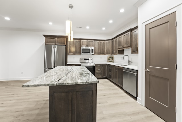 kitchen with appliances with stainless steel finishes, light stone counters, pendant lighting, a center island, and light hardwood / wood-style flooring