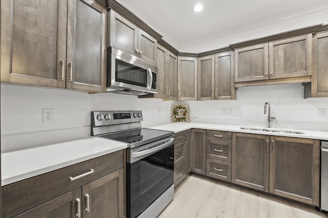 kitchen with appliances with stainless steel finishes, dark brown cabinets, light wood-type flooring, and sink