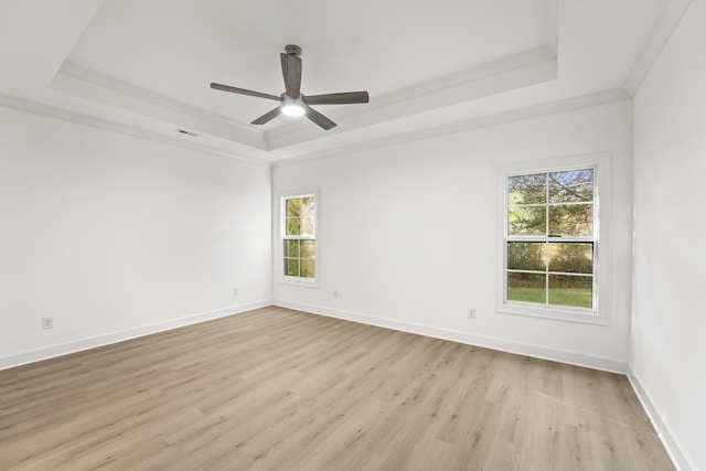 empty room with light hardwood / wood-style flooring, a wealth of natural light, ceiling fan, and a raised ceiling