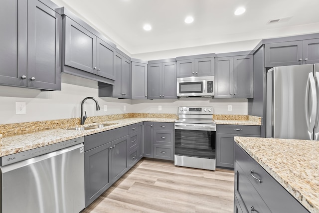 kitchen with appliances with stainless steel finishes, light wood-type flooring, sink, and gray cabinetry