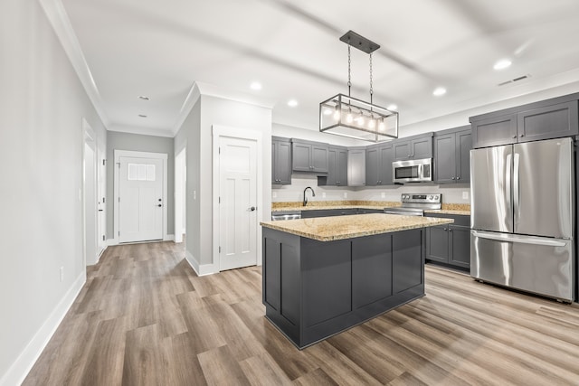 kitchen with appliances with stainless steel finishes, hanging light fixtures, light stone counters, a kitchen island, and light hardwood / wood-style flooring