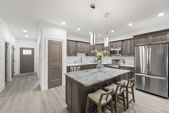 kitchen with stainless steel appliances, light wood-type flooring, a center island, decorative light fixtures, and sink