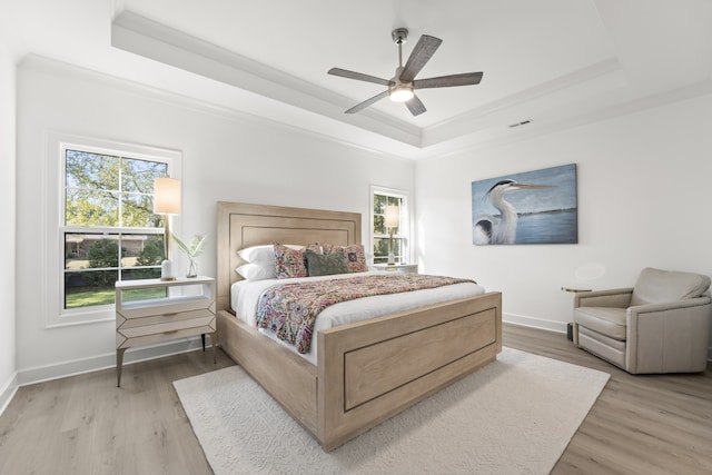 bedroom with ornamental molding, light hardwood / wood-style floors, ceiling fan, and a raised ceiling