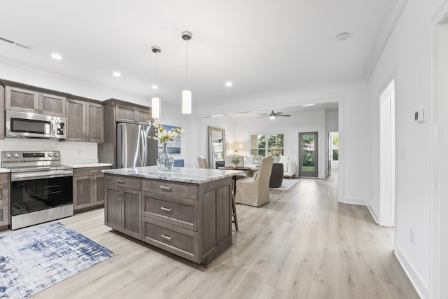 kitchen with ceiling fan, a kitchen island, decorative light fixtures, appliances with stainless steel finishes, and light wood-type flooring