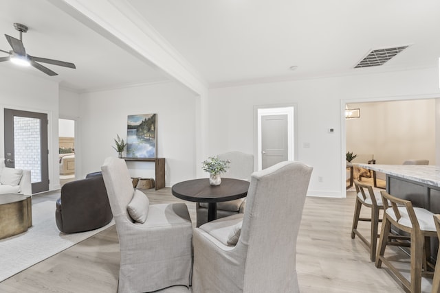 dining room with light wood-type flooring, beamed ceiling, ornamental molding, and ceiling fan