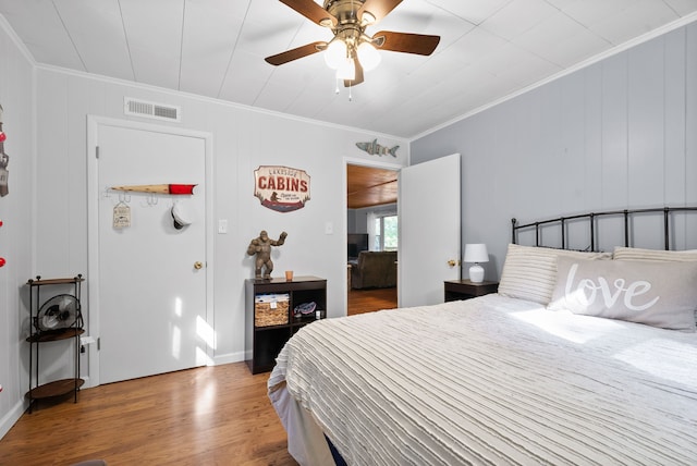 bedroom with wood-type flooring, crown molding, wood walls, and ceiling fan