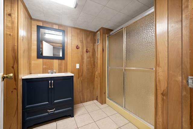 bathroom with wooden walls, tile patterned flooring, a shower with door, and vanity