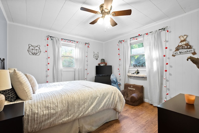 bedroom with ceiling fan, ornamental molding, wooden walls, and hardwood / wood-style floors