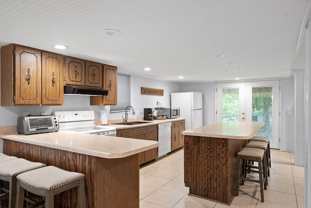 kitchen featuring light tile patterned flooring, kitchen peninsula, sink, white appliances, and a kitchen breakfast bar