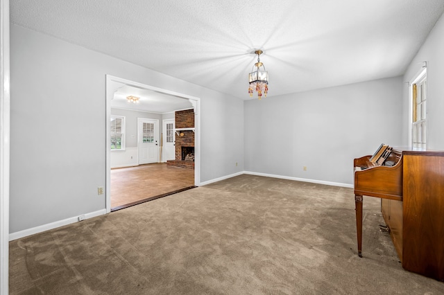 carpeted empty room featuring a brick fireplace and a textured ceiling