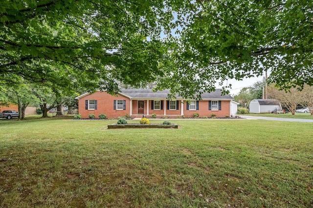 ranch-style home featuring a storage unit, covered porch, and a front yard