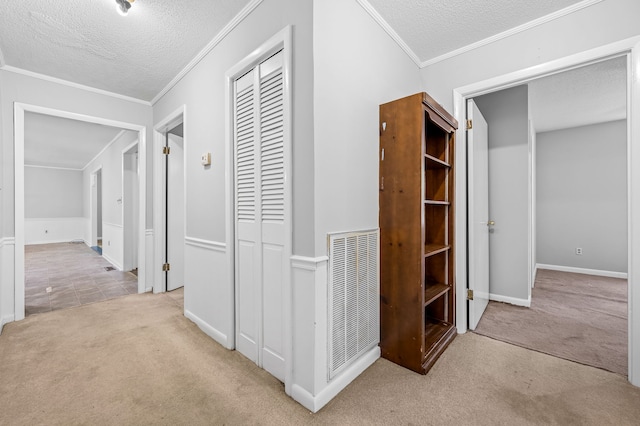 hallway featuring a textured ceiling, ornamental molding, and light carpet