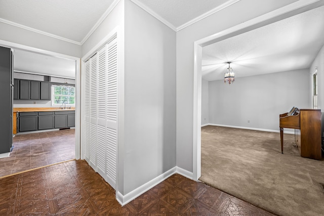 corridor with a textured ceiling, crown molding, dark colored carpet, and sink