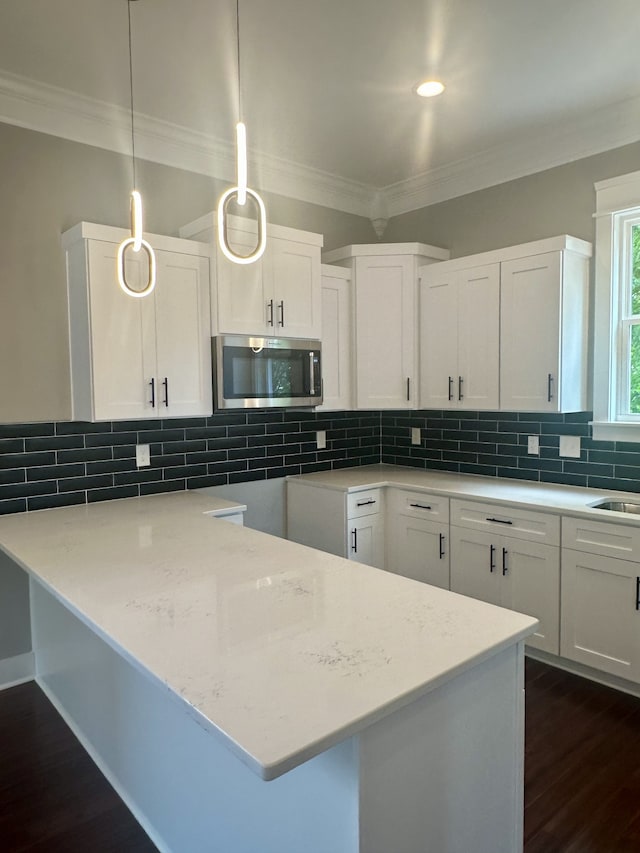 kitchen featuring pendant lighting, dark wood-type flooring, white cabinetry, decorative backsplash, and ornamental molding