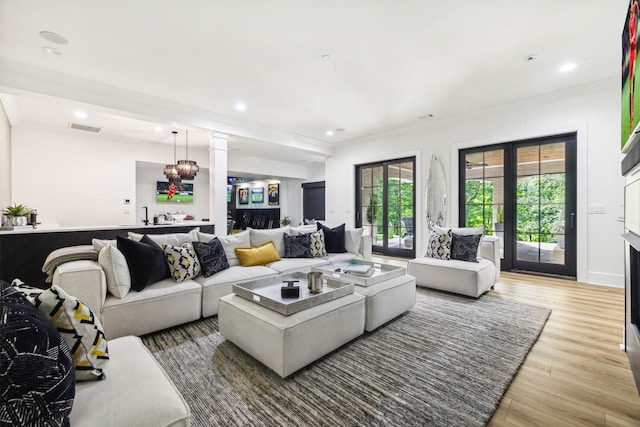 living room with french doors, light wood-type flooring, ornamental molding, sink, and an inviting chandelier