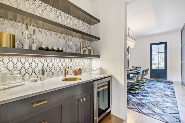 bar with light stone countertops, decorative backsplash, ornamental molding, beverage cooler, and sink