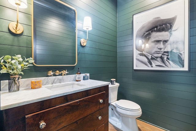 bathroom featuring vanity, toilet, wood-type flooring, and wooden walls