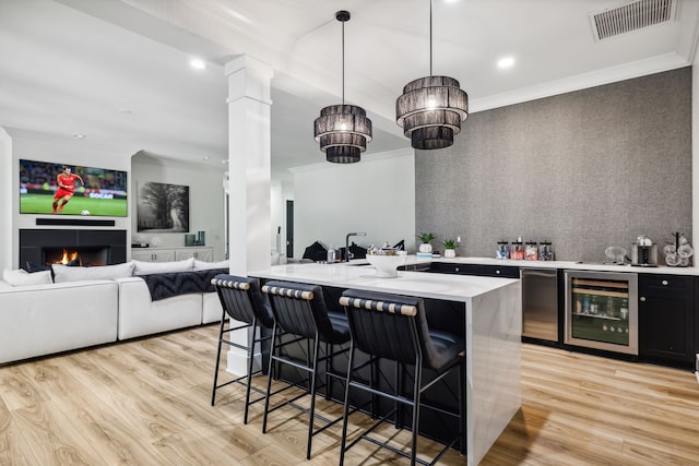 kitchen featuring a breakfast bar, beverage cooler, decorative light fixtures, and light hardwood / wood-style floors