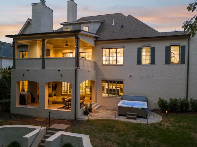 back house at dusk with a patio area, a balcony, and a hot tub