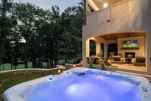 pool at dusk with a patio area, exterior fireplace, and a hot tub