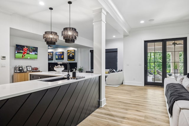 kitchen with decorative columns, crown molding, sink, pendant lighting, and light hardwood / wood-style flooring