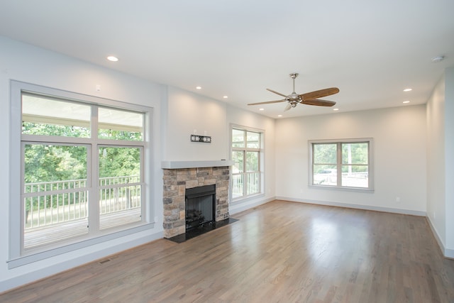 unfurnished living room featuring ceiling fan, a stone fireplace, and hardwood / wood-style floors