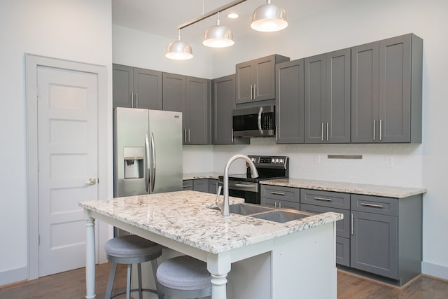 kitchen featuring pendant lighting, gray cabinetry, a center island with sink, appliances with stainless steel finishes, and dark hardwood / wood-style flooring