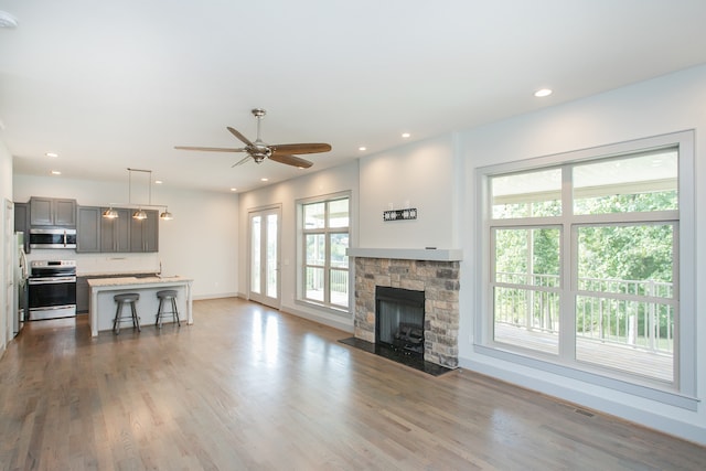 living room featuring light hardwood / wood-style floors, ceiling fan, and a stone fireplace