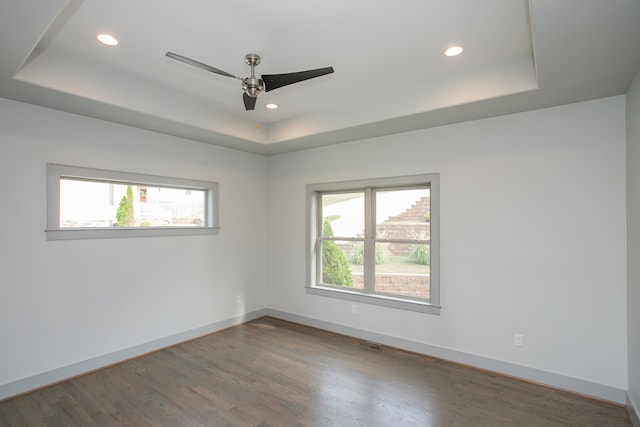 unfurnished room with ceiling fan, a tray ceiling, and dark wood-type flooring