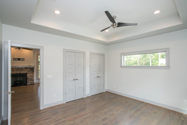 unfurnished bedroom featuring ceiling fan, a fireplace, a raised ceiling, and hardwood / wood-style floors