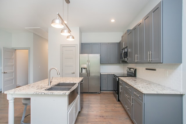 kitchen featuring appliances with stainless steel finishes, light stone countertops, pendant lighting, a center island with sink, and dark hardwood / wood-style floors