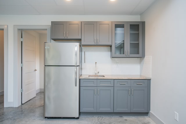 kitchen with light stone countertops, backsplash, gray cabinets, and stainless steel refrigerator